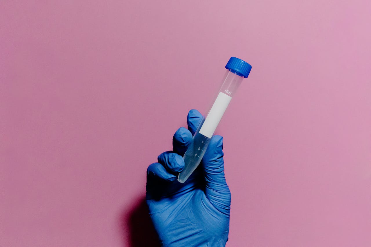 Blue gloved hand holds a test tube against a pastel pink background, emphasizing medical themes.